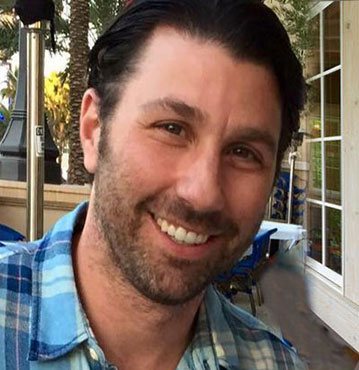 Portrait of Michael Zucker smiling outdoors in a plaid shirt